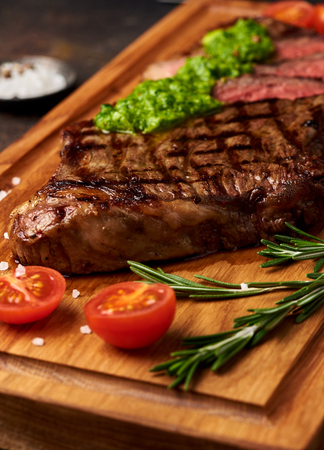 Grilled Black Angus Steak with tomatoes, garlic with chimichurri sauce on meat cutting board.の写真素材