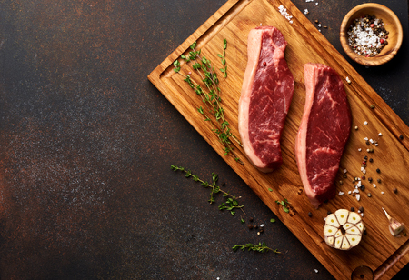 Raw fresh meat Picanha steak, traditional Brazilian cut with thyme, garlic, and black pepper on wooden board. Sliced meat steaks. Copy space. Top view.の写真素材