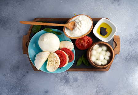 Italian soft cheeses plate. Mozzarella Buffalo, balls, Stracciatella, basil leaves, tomatoes, olive oil with vinegar on gray background. Top view, copy space.の写真素材