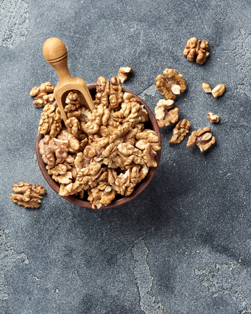 Walnut kernels with wooden scoop on gray background with copy space. Nuts in clay bowl. Top view.の写真素材