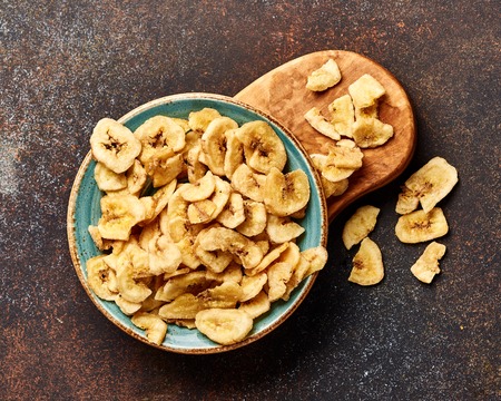 Dried banana slices on brown background. Top view of banana crunchies.の写真素材