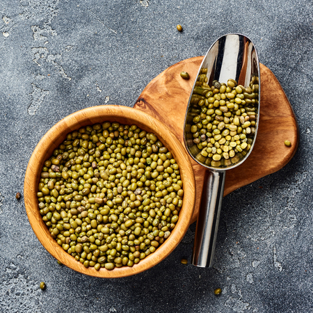 Green mung beans in wooden bowl on gray background. Top view of groats.の写真素材