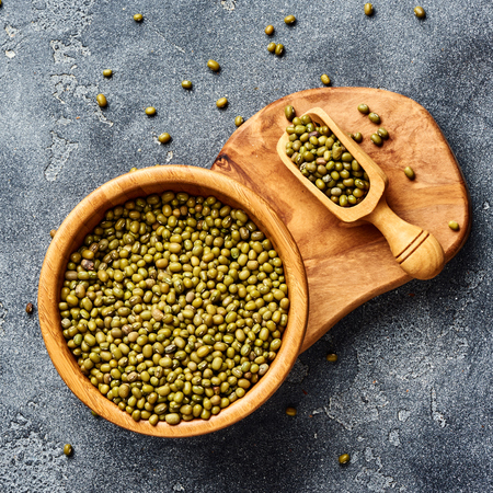 Green mung beans in wooden bowl on gray background. Top view of groats.の写真素材