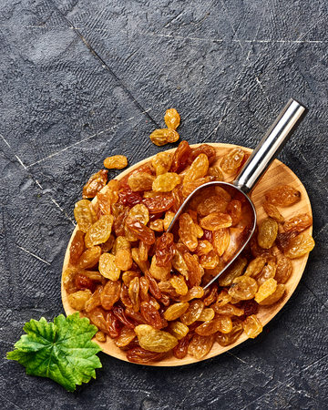 Yellow raisins on black concrete background with scoop. Top view of dried grapes.の写真素材
