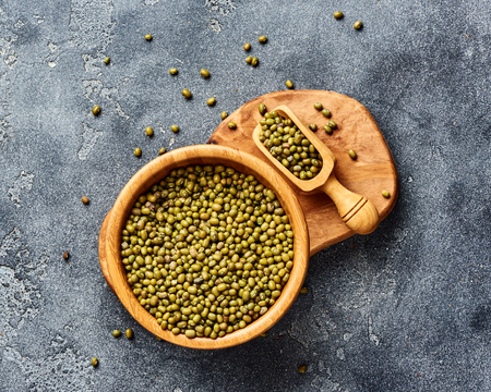 Green mung beans in wooden bowl on gray background. Top view of groats.の写真素材
