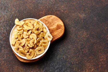 Dried banana slices on brown background. Top view of banana crunchies.の写真素材