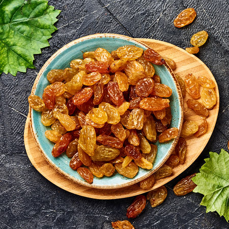 Yellow big raisins on black concrete background. Top view of dried grapes.の写真素材