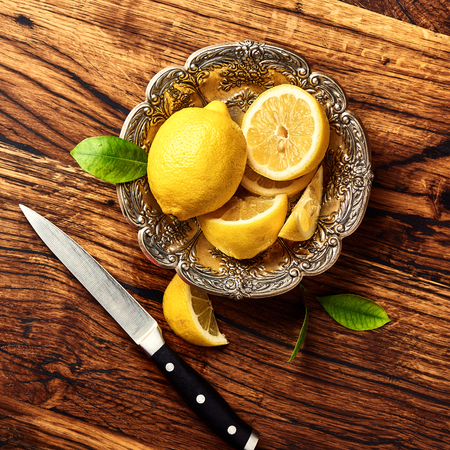 Lemons with leaves on oak wooden table. Top view of fruits with knife.の写真素材