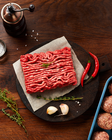 Minced beef meat and meatballs with salt, garlic, herbs on wooden table. Top view.