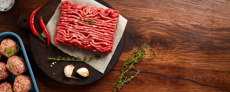 Minced beef meat and meatballs with salt, garlic, herbs on wooden table. Top view. Copy space for...