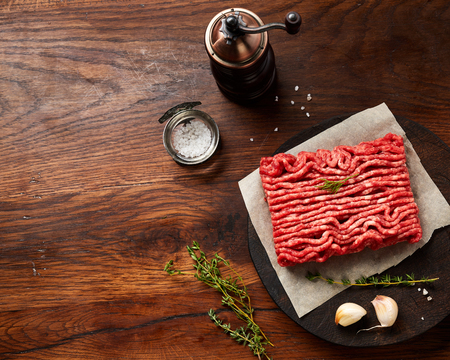 Minced beef meat with salt, garlic, herbs on wooden table. Top view.の写真素材