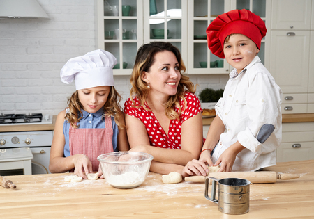 Happy mother with funny kids are preparing the dough, bake cookies in the kitchenの写真素材