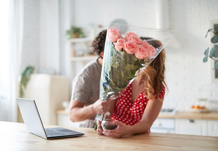 Summer holidays, love, relationship - couple with bouquet of flowers in the kitchen. Laptop on the table.の写真素材