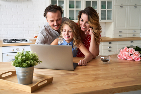 Young happy family surfing internet with laptop on table at kitchenの写真素材