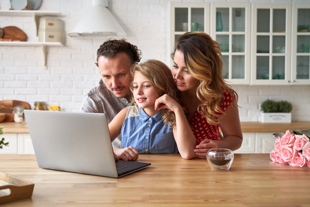 Young happy family surfing internet with laptop on table at kitchenの写真素材