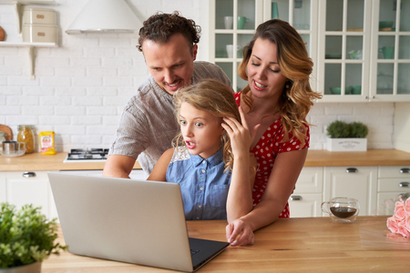 Young happy family surfing internet with laptop on table at kitchenの写真素材