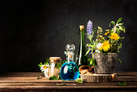 Homeopathy and Alternative Medicine. Healing Herbs in stone mortar and Essential Oil in Glass Bottles. Crushed healing herbs on wooden table.の写真素材