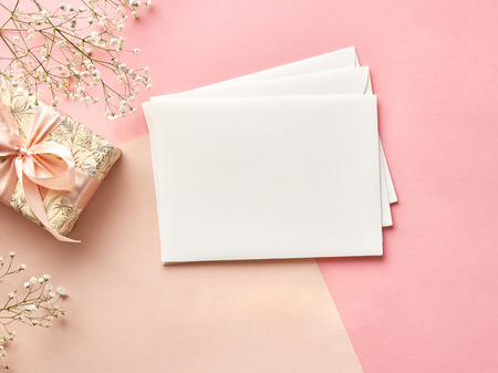 Mock up of blank envelopes on pink or beige background with flowers and present. View from the top.の写真素材