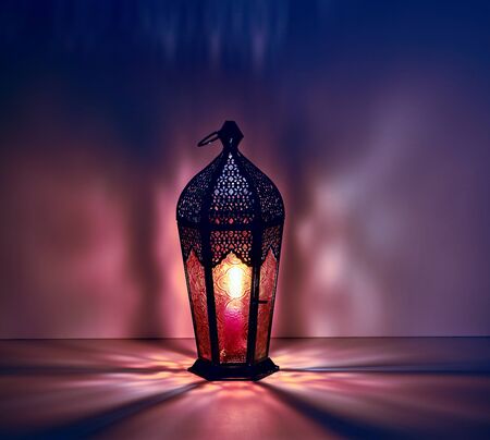 Ramadan lantern on the table. Dark background with blue and purple light. Beautiful Greeting Card with copy space for Ramadan and Muslim Holidays. An illuminated Arabic lamp.の写真素材