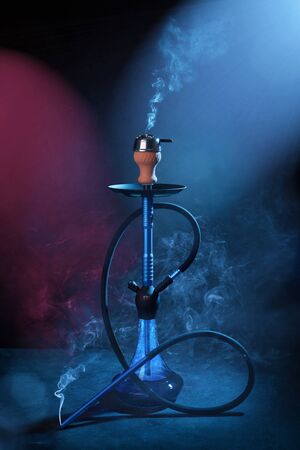 Smoking a hookah on a dark blue background, with smoke and neon lightの写真素材