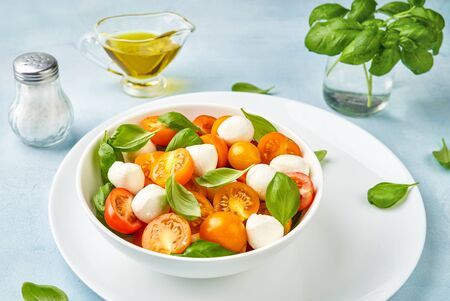 Salad with yellow tomato cherry and mini mozzarella cheese in white bowl on white plate. Bocconcini mozzarella cheese with fresh basil leaves in caprese salad.の写真素材