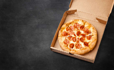 Pizza in a cardboard box on a dark chalkboard. Space for your text. Top view of pizza package. Pizza delivery.の写真素材