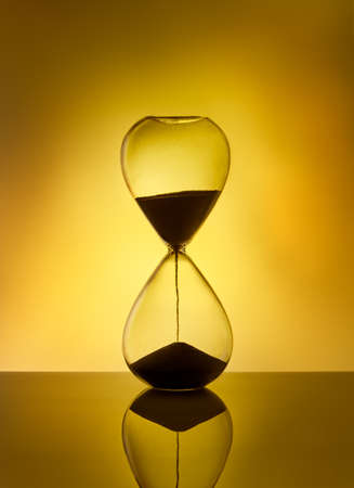 Hourglass as time passing concept for deadline, running out of time. Sandglass on yellow background. Concept of urgency.の写真素材