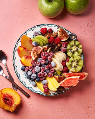 Assorted sliced fruits on vintage plate. Top view of mango, kiwi fruits, figs, grape, bananas, green apples, peach fruit, raspberries and blueberries on pink background.の写真素材