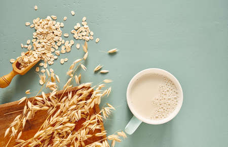 Oat milk in a glass and mug on a blue background. Flakes and ears for oatmeal and granola on a wooden plate.の写真素材