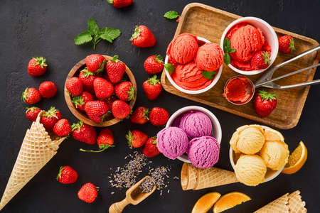 Heap of strawberry and orange, dried lavender with cups of ice cream and cones. Lavender, strawberry and orange sorbet on black background.の写真素材