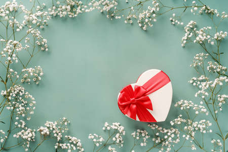 Flowers composition with gift. White flowers on turquoise blue background and shaped heart gift....