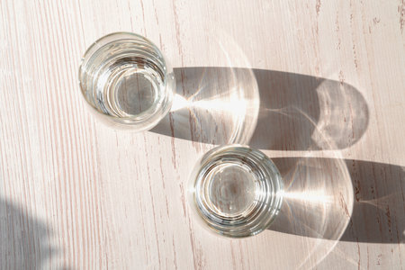 Two glasses of water on white wooden background under direct sun shines. Top view of glasses water. Caustic reflection effect.の写真素材