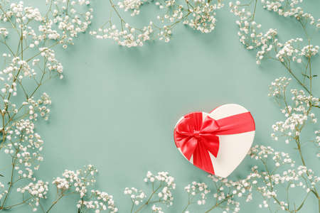 Flowers composition with gift. White flowers on turquoise blue background and shaped heart gift. Wedding mockup with small flowers and gift with a red bow. Flat lay, top view, frame. Gypsophila Baby's-breath flowersの写真素材