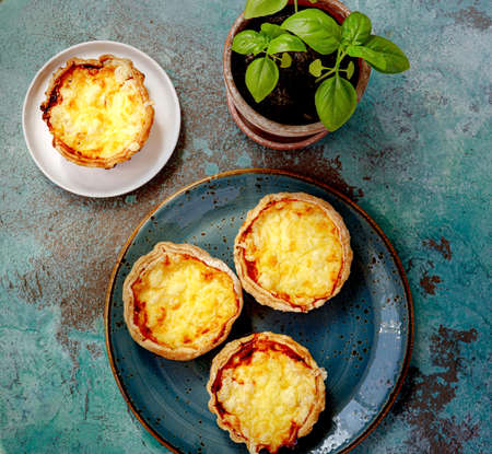 Mini quiches on a blue plate. Flaky dough pies. Fresh basil and mini quiches on a blue background.の写真素材