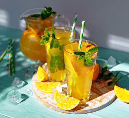Glasses of lemonade with lemons, oranges and mint leaves on blue wooden background. Summer cold drinks under direct sun shines.の写真素材