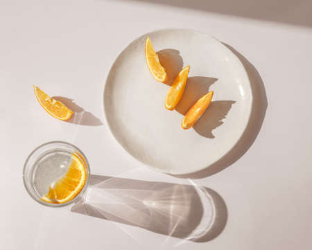 Sliced orange with glass of water and sharp shadows stands on light pink background. Top view flat lay. Caustic reflection effect. Modern trendの写真素材
