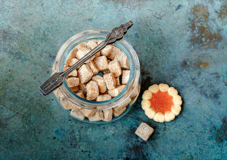 Bowl of cane sugar cubes with sugar tweezers and sweet cookies on blue vintage background.の写真素材