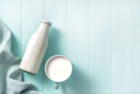 A bottle of milk and mug of milk on a wooden table. Top view of milk on a blue backgroundの写真素材