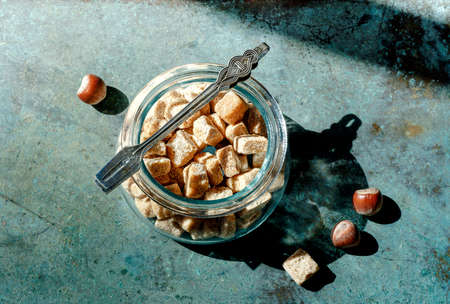 Bowl of cane sugar cubes with sugar tweezers and haselnuts on blue vintage background.の写真素材