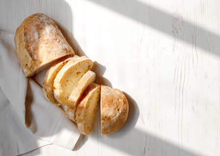 Sliced organic bread ciabatta with vintage linen napkin on white wooden background. Top view of homemade ciabatta. Flat lay.の写真素材