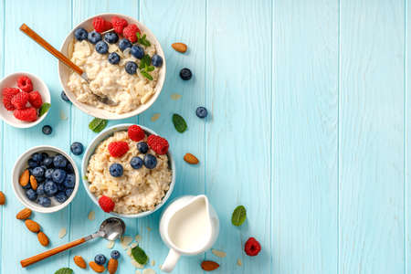Bowls of oatmeal porridge with blueberries and raspberries on blue table. Top view flat lay. Healthy breakfast and diet food. Porridge with fresh berries and almond slices.の写真素材