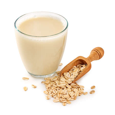 Glass of oat milk with oat flakes in wooden spoon isolated. Gluten free oat milk on white backgroundの写真素材