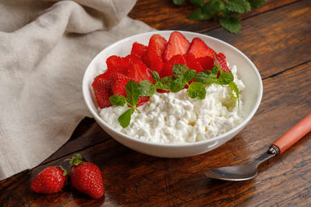 Soft cheese with strawberries in white bowl on wooden table.の写真素材