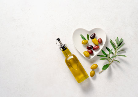 Fresh olives on a white plate in the shape of a heart and branch of olive on white background. Bottle of olive oil. Mockup for package. Copy space.の写真素材