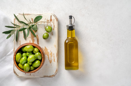 Olives, olive oil in bottle and branch of olive on white wooden board. Mockup for package. Copy space.の写真素材