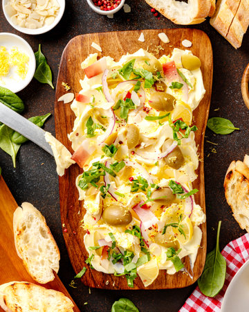 Homemade trendy butter board with onion, olives, herbs and bread. Butter board with toasts on dark background. Top view.の写真素材