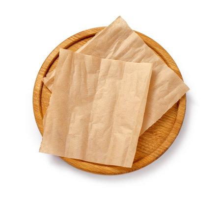 Baking paper on wooden board isolated. Round board with crumpled pieces of brown parchment or baking paper on white background. Top view. Design element.の写真素材