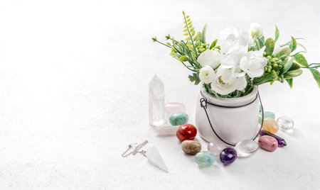 Gemstones for esoteric spiritual practice. Reiki therapy concept. Feng Shui, Healing Crystal Ritual, Witchcraft, Relax Chakra, litho therapy. Crystals and rock crystal pendulum with white flowers on the table.の写真素材