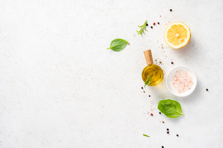 Various herbs and spices, oil in glass bowl and half of lemon on a white concrete background. Background for recipe, menu, textの写真素材