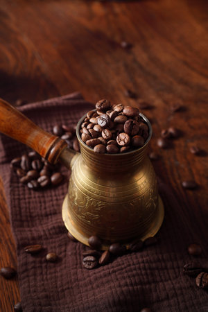 Coffee beans in the turkish dzezva coffee pot on wooden background with brown kitchen napkin. Top view.の写真素材